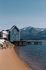 Fototapeta premium Blue lakeside house on stilts by a sandy beach with mountain view for waterfront wallpaper and background design