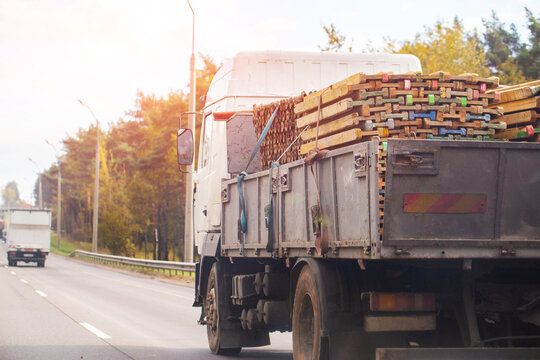 Large white flatbed truck transporting construction wood materials on highway road with sun flare, delivery service