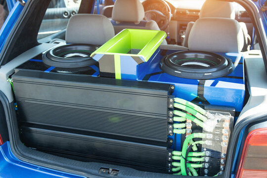 Custom car audio system installation in open trunk of blue vehicle showing powerful subwoofers, multiple amplifiers, and intricate wiring setup for enhanced sound experience