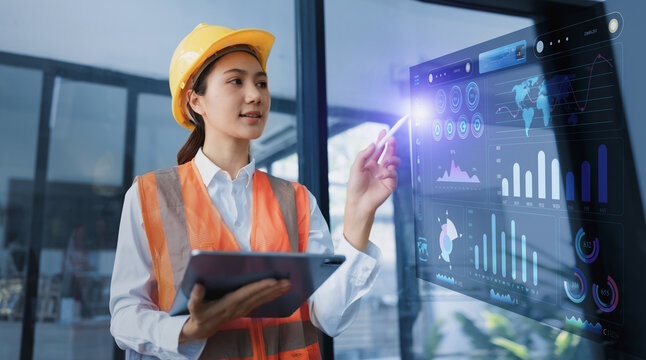 A female engineer in a yellow hard hat and orange safety vest holds a tablet and interacts with digital interface data and connectivity.