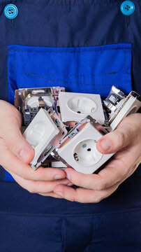 Person hands holding collection of electrical power sockets, new white plastic wall outlets with metal frames, blue work uniform background, ready for installation or repair, vertical photo