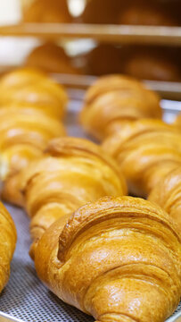 Rows of freshly baked golden brown croissants on metal tray display in warm light from bakery oven creating inviting breakfast or snack scene vertical photo