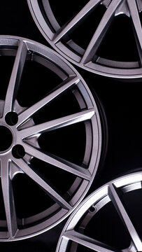 Three new silver gray metallic aluminum alloy car rims wheel spokes design automotive part black background closeup studio light vertical photo