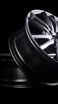 Modern dark grey alloy car wheel rims stacked, showcasing sleek design and metallic finish of spokes against black background for automotive concept vertical photo
