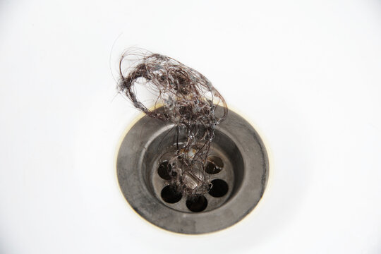 Messy tangle of dark human hair collected on top of metal bathroom sink drain, clearly indicating plumbing blockage, water drainage issue and immediate need for cleaning, copy space
