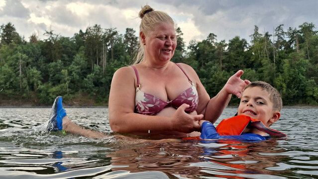 Grandmother teaches her grandson to swim in the lake. They enjoy their summer vacation on the water together.