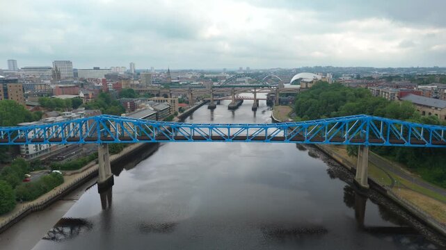 The blue Queen Elizabeth II Bridge over River Tyne and urban Newcastle skyline under cloudy weather, North England