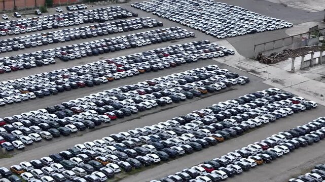 Drone lateral slide reveals a large automotive storage yard with long rows of parked passenger vehicles awaiting distribution across a paved vehicle logistics terminal, drone lateral slide.