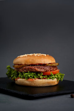 Juicy double cheeseburger with two meat patties, melted cheddar, pickles, and lettuce on black slate board, dark background.