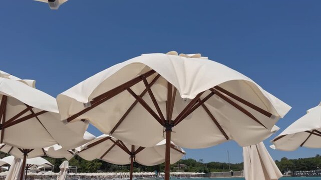 Close up view of large canvas beach umbrellas with wooden frames standing against a bright clear blue sky background