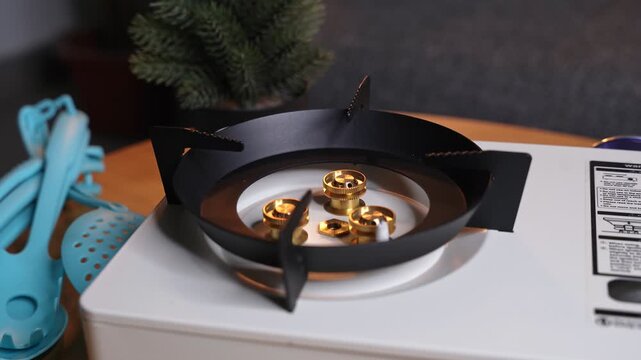 Close up shot of a blue gas flame igniting on a white portable stove. The burner sits on a wooden table next to blue kitchen utensils in a modern indoor home setting with a shallow depth of field.