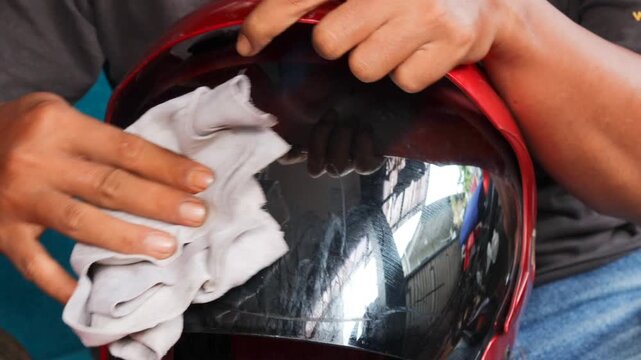 Close-up of a man cleaning a motorcycle helmet visor with a microfiber cloth at home before riding, removing dust and smudges as part of routine helmet maintenance.