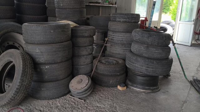 Inside an auto repair shop with tall stacks of used car tires, a red hydraulic jack, and a tire changer. Authentic garage environment perfect for automotive maintenance and auto service concepts.