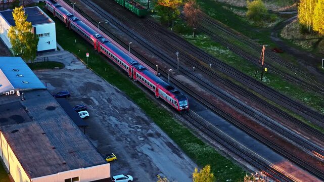 Modern electric passenger train stopped at a railway station platform in aerial vew during golden hour