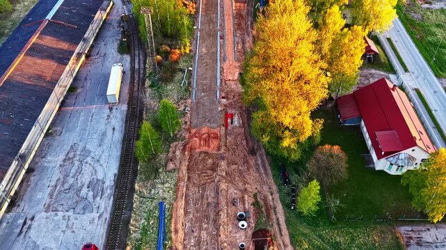 New street under construction next to a railroad track at sunset, top-down aerial view