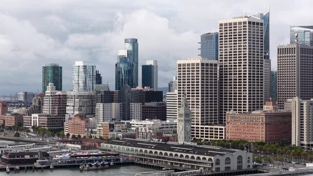 Morning drone shot captures the iconic San Francisco waterfront, featuring the Ferry Building, modern skyscrapers, and calm bay under dramatic sunrise clouds. Tracking aerial footage.