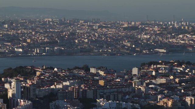 Stunning aerial footage glides over Lisbon and Almada at golden hour, revealing vibrant urban architecture, shimmering Tagus river, and distant city skyline under warm sunset light.