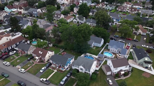 Round above-ground pools dot backyards of closely spaced houses in dense suburban neighborhood, mature trees plus parked cars lining streets in Belleville, New Jersey. Aerial drone top down