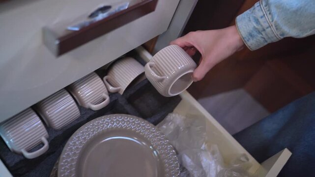 Close-up of a woman's hands carefully arranging ceramic plates and cups in a custom-fitted drawer, showcasing organized storage solutions for compact living spaces in a modern rv