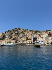 Fototapeta premium Iconic Symi Island harbor with vibrant pastel houses, sparkling turquoise sea, luxury yachts, Mediterranean sunshine, breathtaking aerial and waterfront travel view