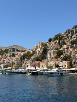 Iconic Symi Island harbor with vibrant pastel houses, sparkling turquoise sea, luxury yachts, Mediterranean sunshine, breathtaking aerial and waterfront travel view