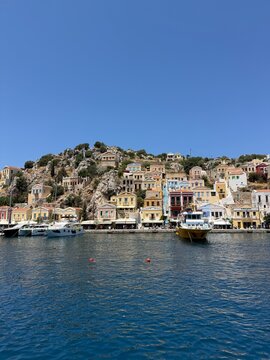 Iconic Symi Island harbor with vibrant pastel houses, sparkling turquoise sea, luxury yachts, Mediterranean sunshine, breathtaking aerial and waterfront travel view
