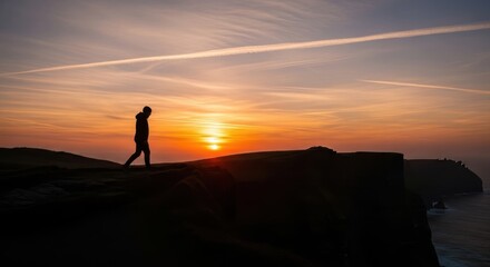 Obraz premium Solitary Wanderer's Silhouette Against a Fiery Sunset Over the Ocean Reflecting on Life's Journey and the Vastness of Nature.