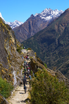 Large group of adventurous tourists trekking along narrow mountain cliff path on iconic route to Everest Base Camp in Nepal Himalayas.
