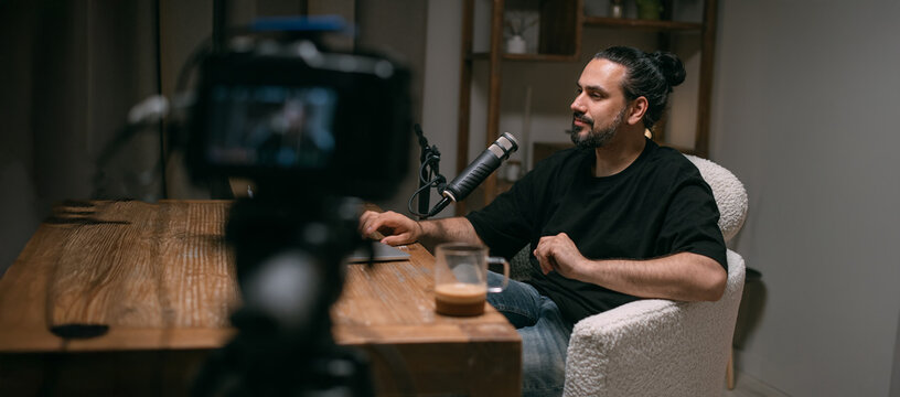 Video podcast recording studio. A young man is sitting at a table in front of a microphone in the frame. The host of the program is filming an episode of the Internet show.