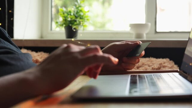 Close-up of hands using credit card for online shopping on laptop