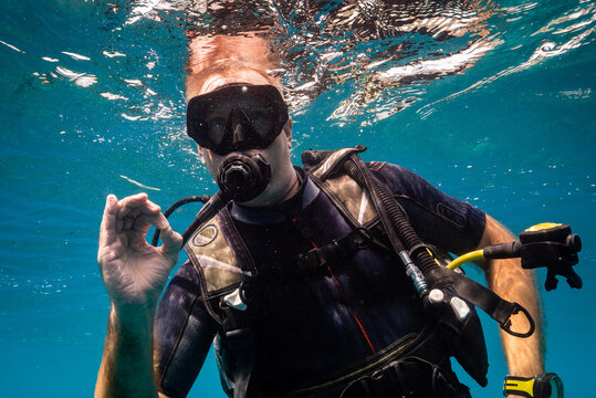 Caucasian male Scuba diver deflating BCD to start dive, with beautiful blue water, wet suit and dive computer, blowing bubbles