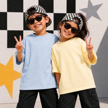 Girl and boy in sunglasses and caps posing by wall. Kids short sleeve tee template. Blue and yellow oversized shirt design for friends, siblings, cousins. Children t-shirt mockup, summer outdoors