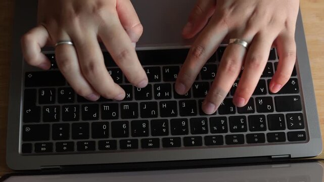 Close-up of hands typing on a laptop keyboard with a ring on one finger