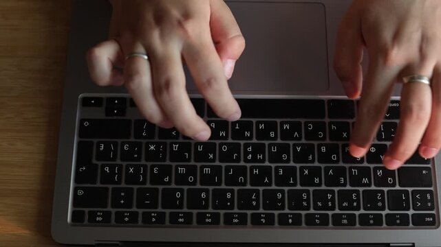 Close-up of hands typing on a laptop keyboard with a wooden desk background
