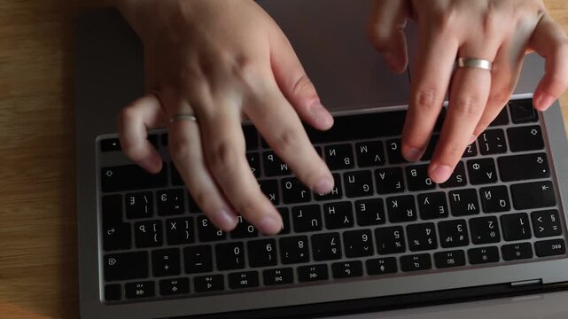 Close-up of hands typing on a laptop keyboard with a wooden desk background