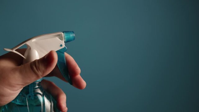 Hand spraying cleaning liquid from a blue bottle with a white trigger sprayer