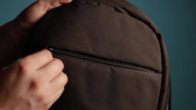 Close-up of hands zipping up a dark brown backpack pocket