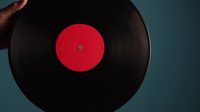 Close-up of a hand holding a black vinyl record with a red label