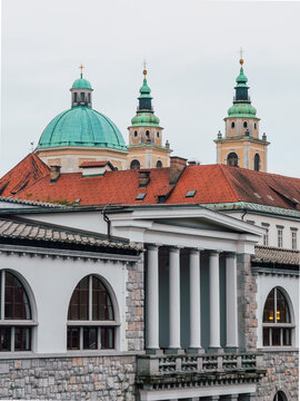 The historic Central Market building along the Ljubljanica River with the green domes and towers of Ljubljana Cathedral in the background.