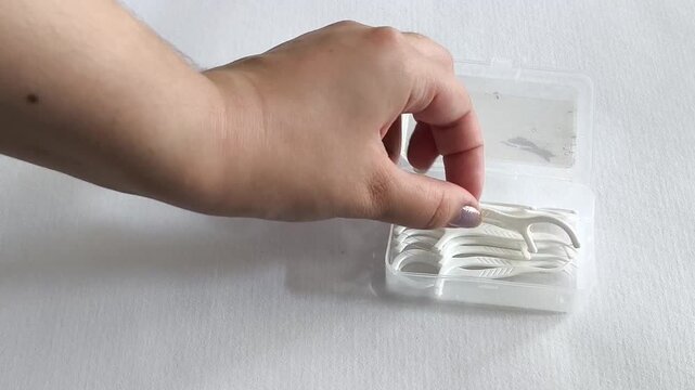 Hand taking dental flosser from container, woman holding floss pick for cleaning between teeth, oral hygiene and dental care.