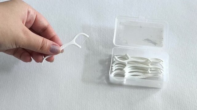 Hand taking dental flosser from container, woman holding floss pick for cleaning between teeth, oral hygiene and dental care.
