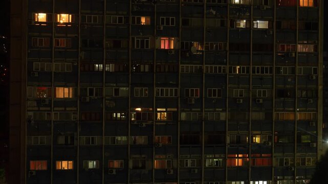 Night facade of a large apartment building with multiple floors where the lights in the windows randomly turn on and off, suggesting the daily life of the residents inside the apartments time lapse