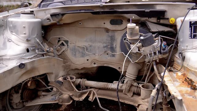 Silver car completely dismantled after a serious road accident, showing the empty engine bay, suspension, steering rack, and brake system, waiting for recycling at a scrapyard or junkyard