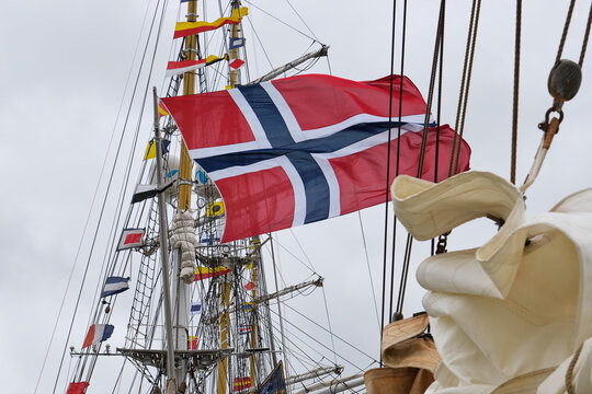 A detailed view of a Norwegian flag fluttering dynamically on a boat's mast against a backdrop of overcast weather conditions	