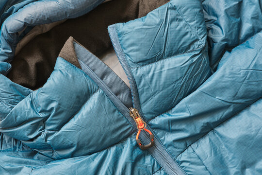 Closeup of a blue down puffer winter jacket with orange details and zipper	