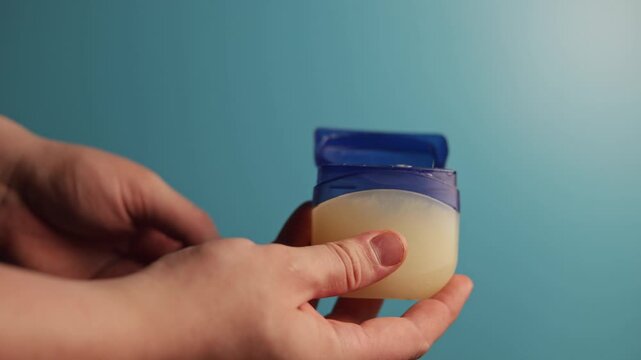 Close-up of hands opening a petroleum jelly jar against a blue background