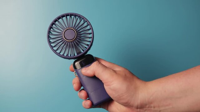 Close-up of a portable purple fan with a gold accent against a blue background