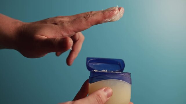 Close-up of hand applying petroleum jelly from a blue container