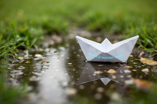 Small paper boat floating in rain puddle on grass with childhood, adventure