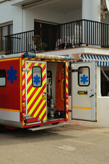 Ambulance vehicle with open rear doors showing medical equipment inside, parked near a residential building during an emergency call. © Ekaterina